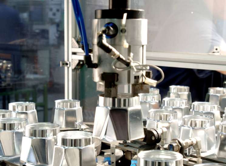 Bialetti Moka espresso makers on an assembly line with industrial machinery and blue tubing.