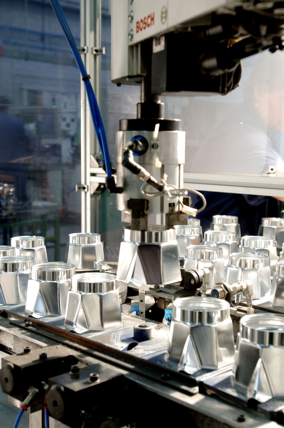 Bialetti Moka espresso makers on an assembly line with industrial machinery and blue tubing.