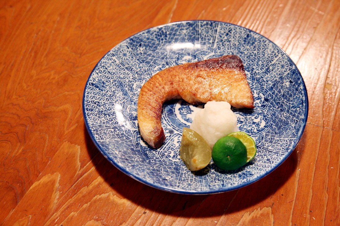 Grilled buri (yellow tail) with salt, daikon radish, and lime on a blue and white patterned plate.