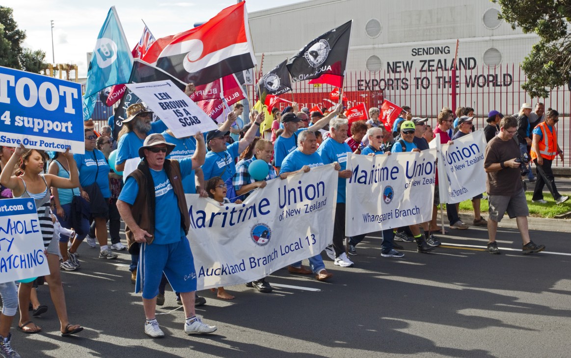 Maritime Union workers protest outside Auckland port with flags and banners during strike action.