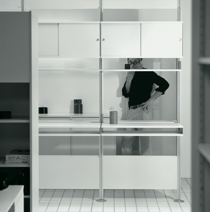 Person viewed through glass shelving unit of Dieter Rams' 606 shelving system.