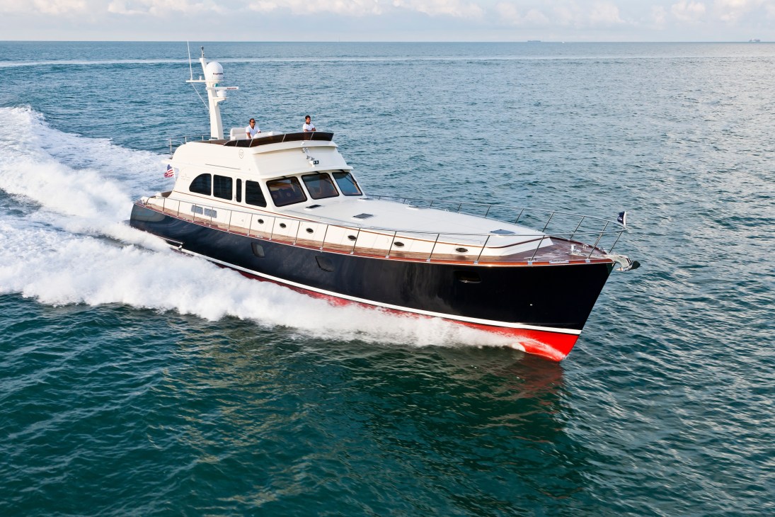 A white and black motor yacht with mahogany hull approaching shore in shallow waves.