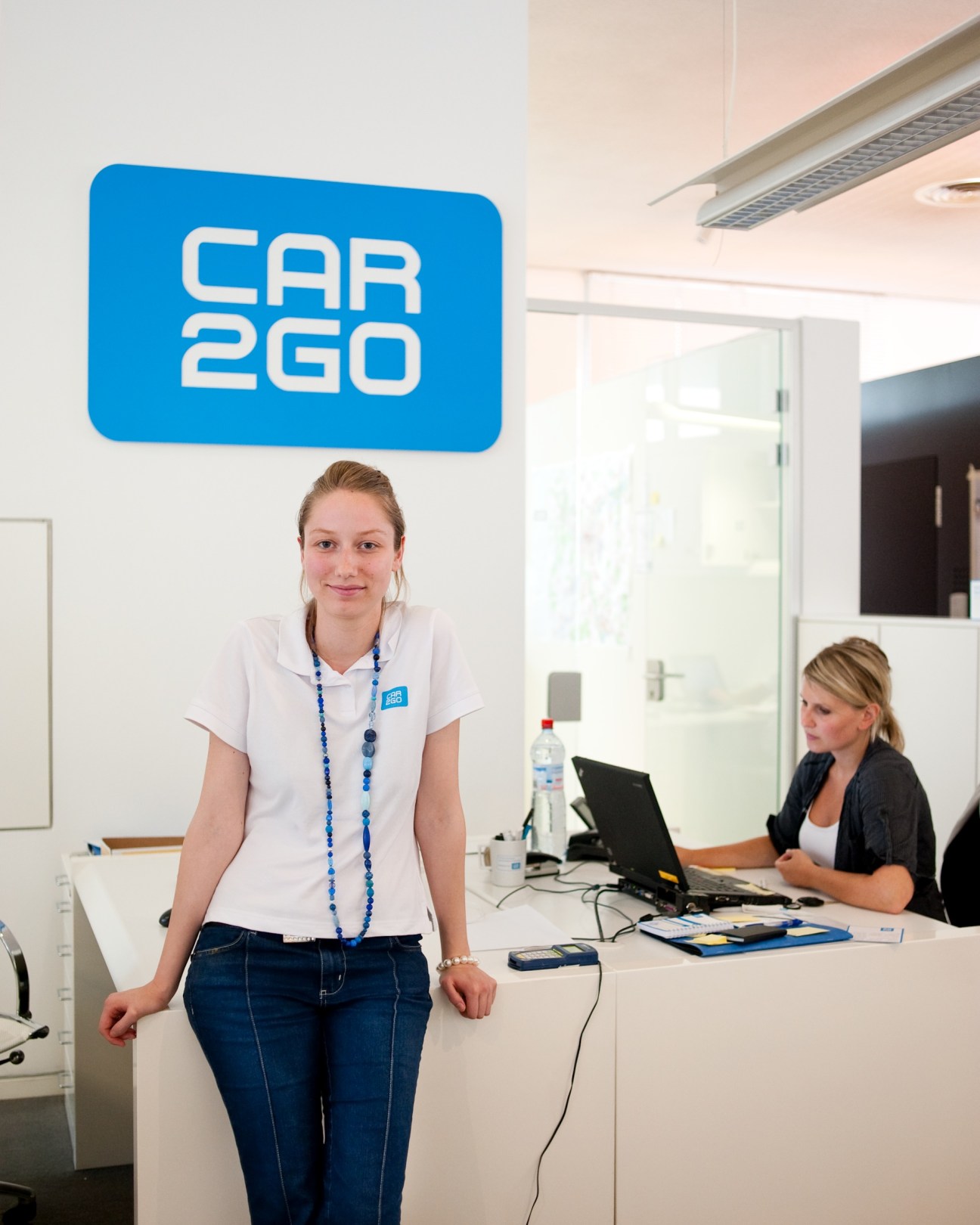 Car2go employee at reception desk with blue Car2go logo on wall behind her.