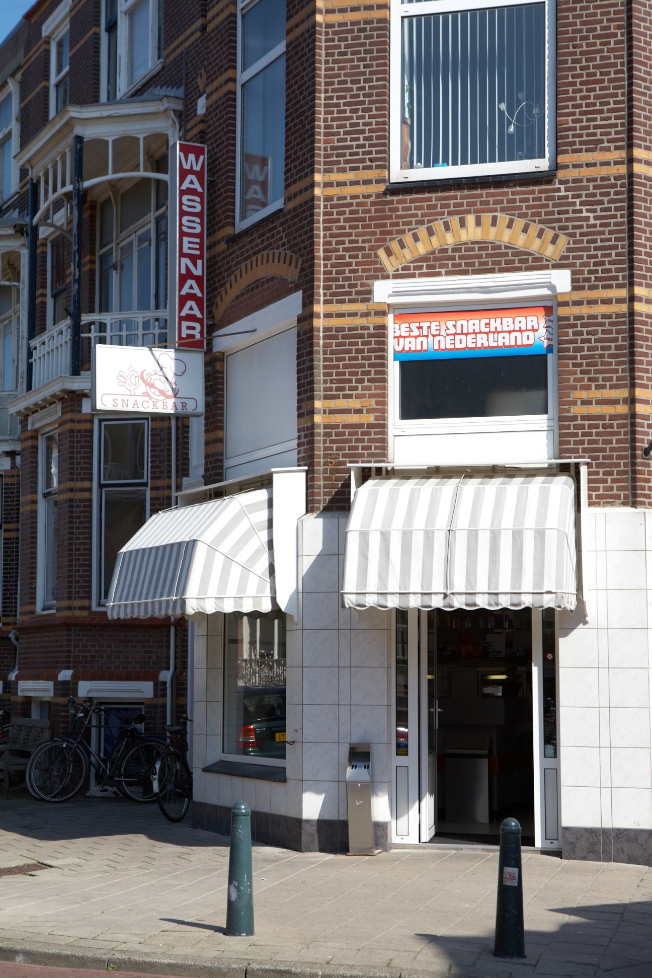 Exterior of Wassenaar Snacks snack bar with brick façade and striped awning in Scheveningen.