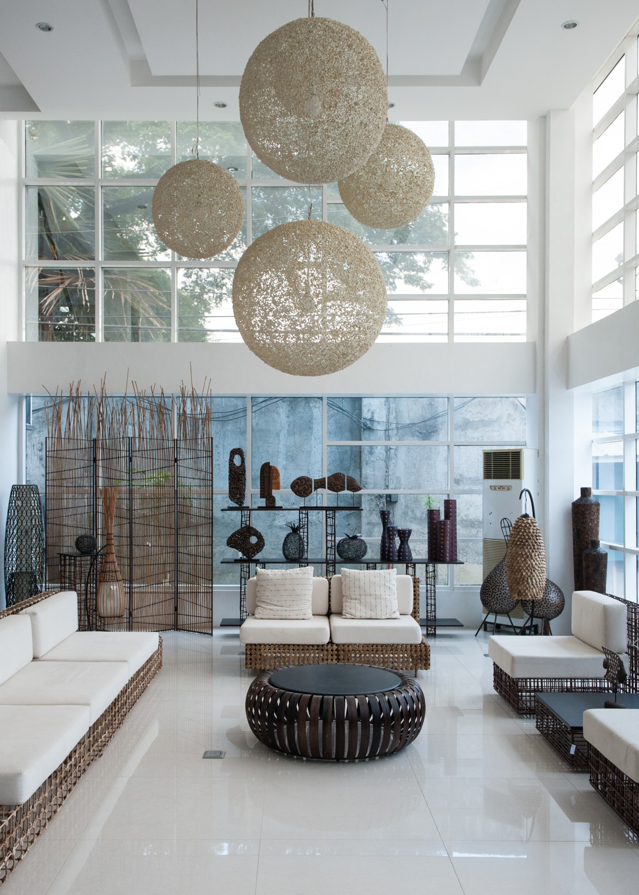 Modern showroom with woven sphere pendant lights, rattan furniture, and woven accessories displayed on shelves.