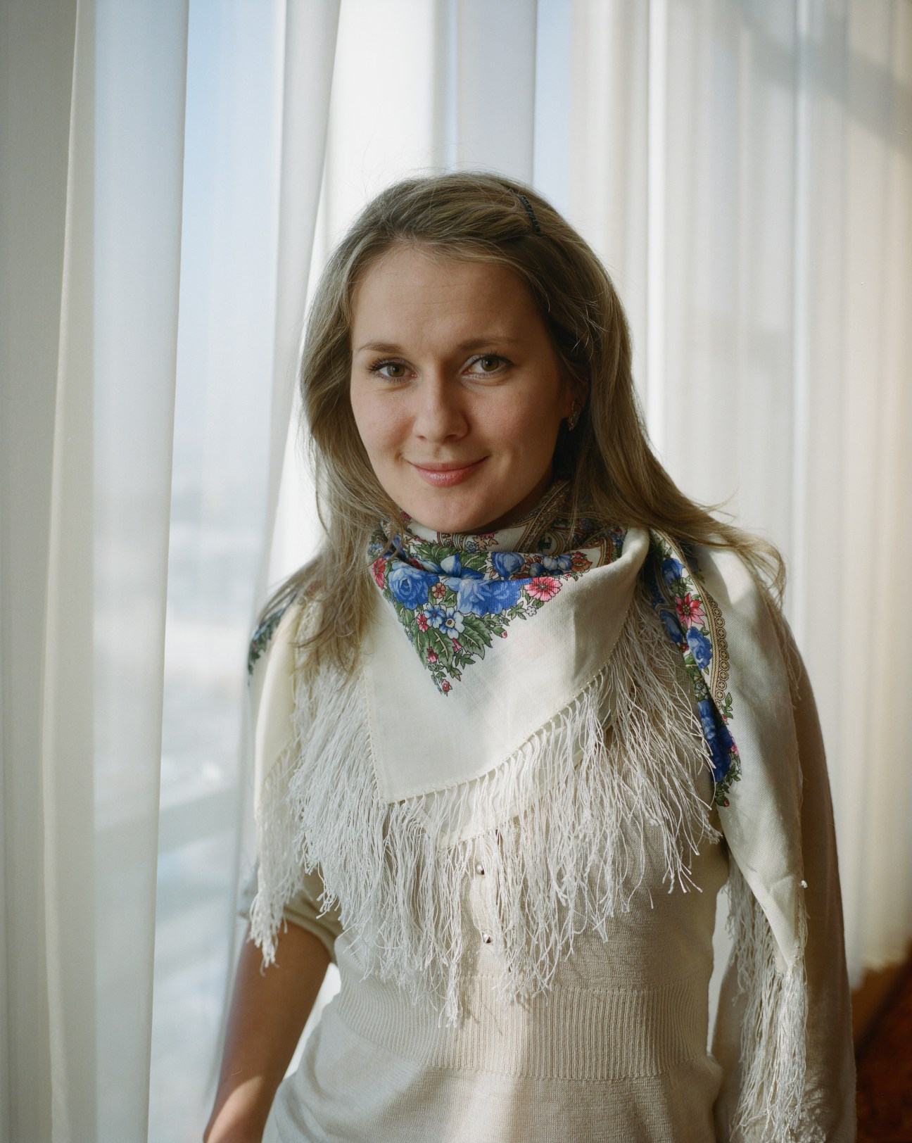 Svetlana Kostromitinova, a mining analyst, poses by a window wearing a cream fringed shawl and floral scarf.