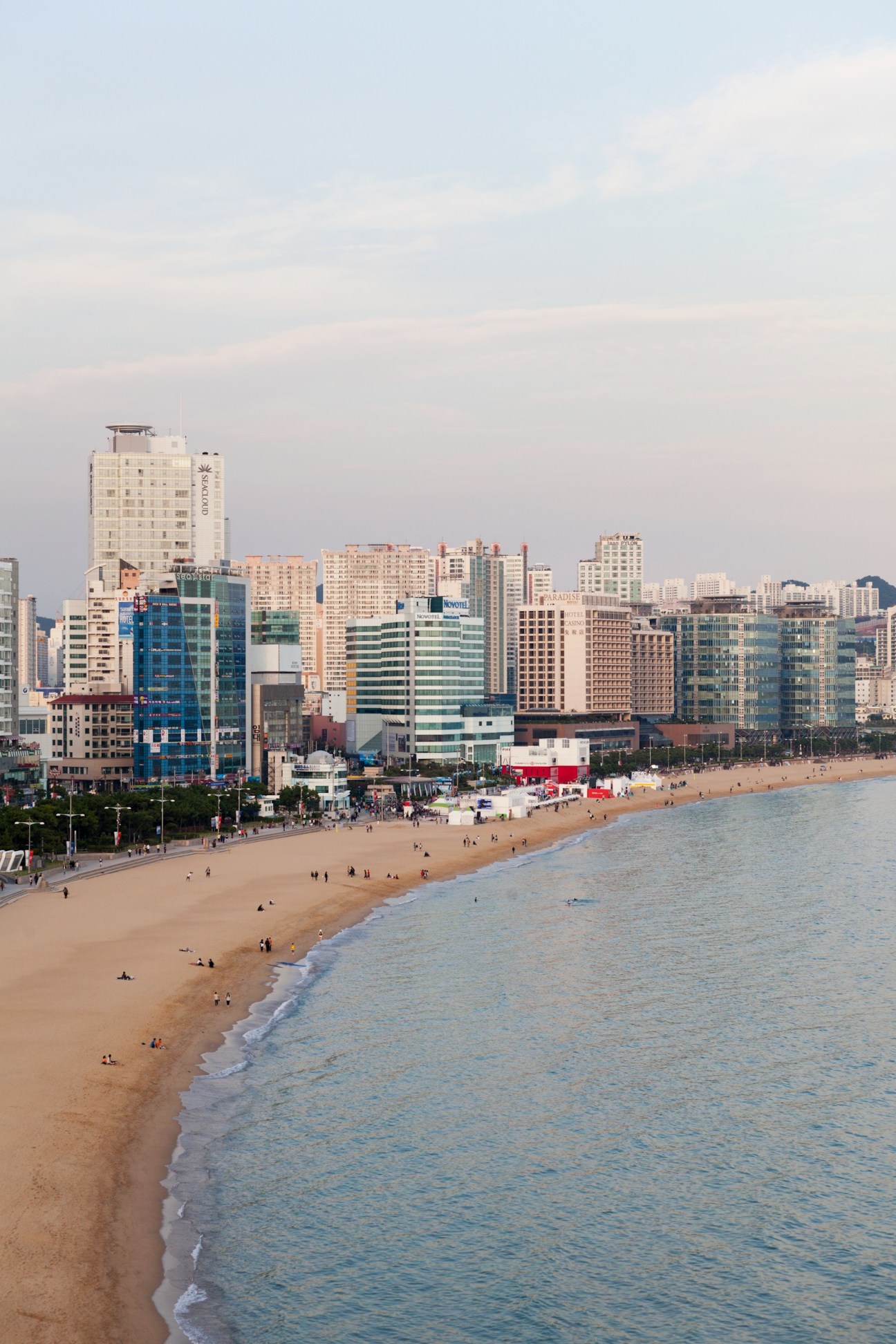 Haeundae Beach in Busan with sandy shoreline, waterfront hotels and high-rise buildings under a hazy sky.