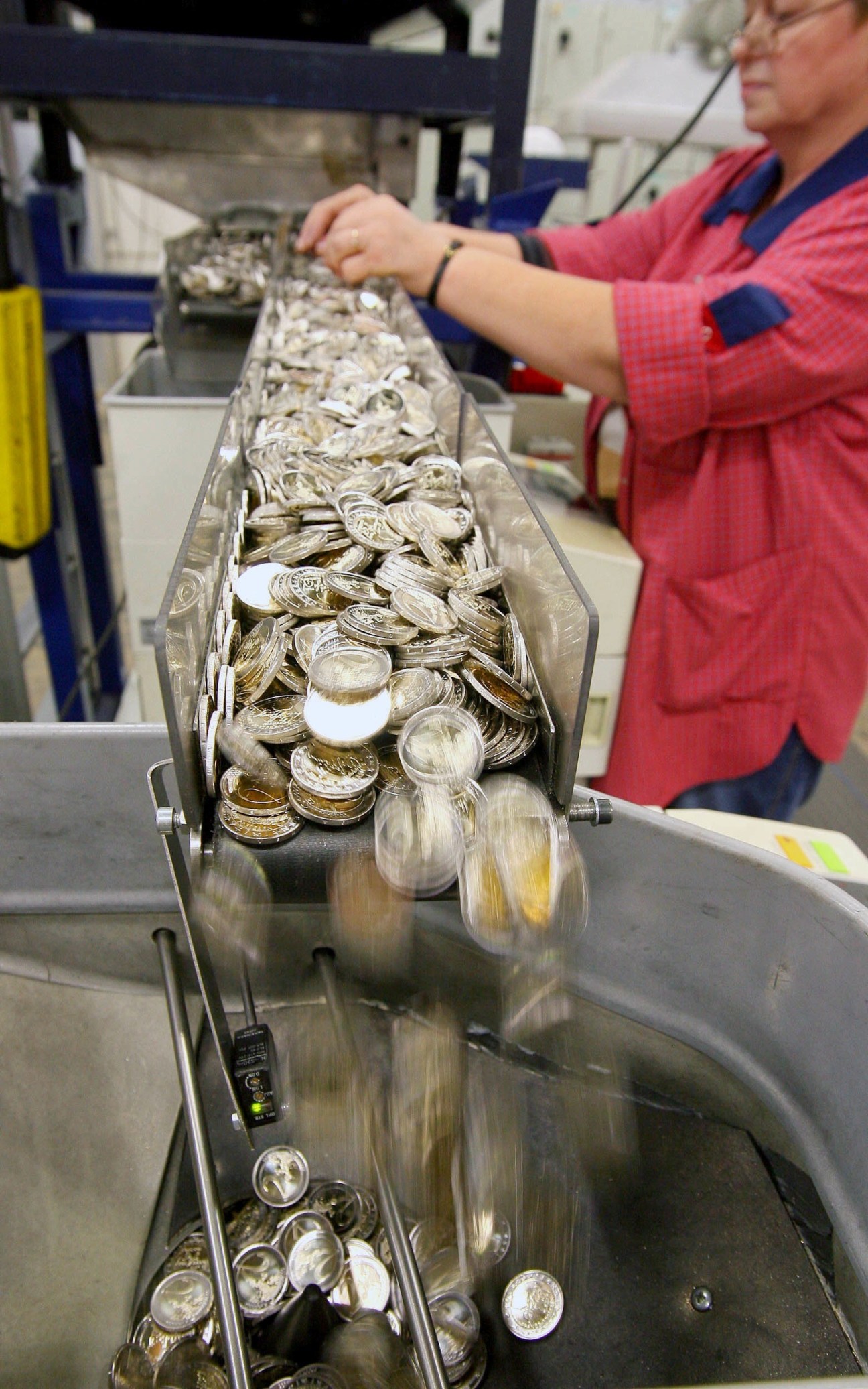 Worker in red jacket sorting euro coins on a production line at the Mint of Finland.