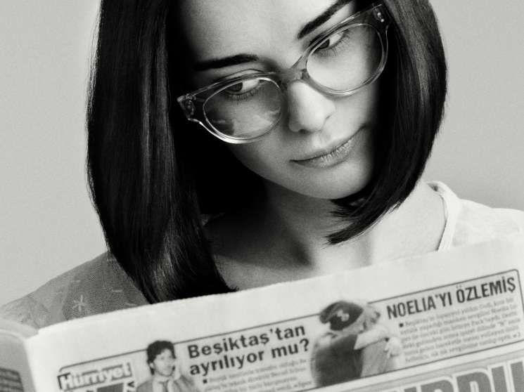 Woman wearing clear-framed Claire Goldsmith Irwin glasses reading a Turkish newspaper in black and white.