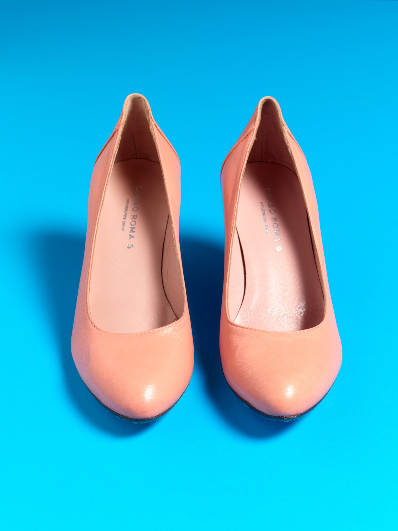 Pair of salmon pink napa-leather mid-heel kitten heels by Corso Roma 9 against a bright blue background.