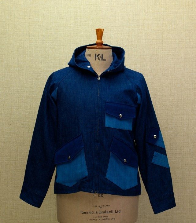 Navy blue jacket with lighter blue pockets displayed on a dress form against a cream background.
