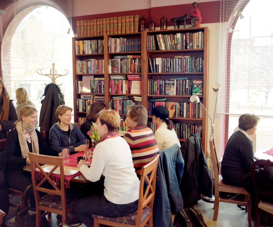 Customers gather inside Cafe & Eepos, a casual café with wooden furniture and bookshelves lining the walls.