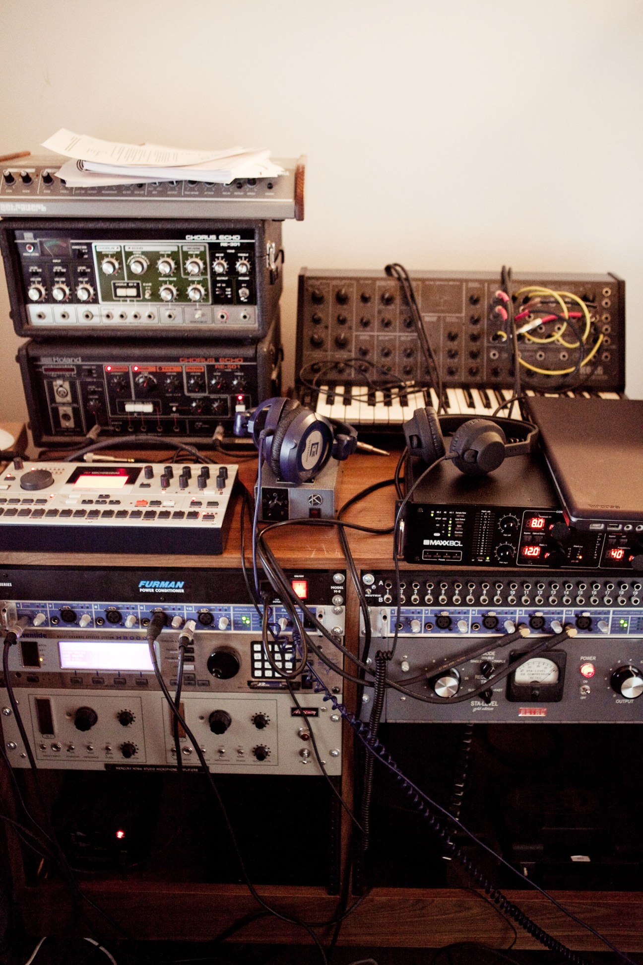 Electronic music production equipment including synthesizers, drum machines, and mixing consoles with headphones in Matthew Dear's studio.