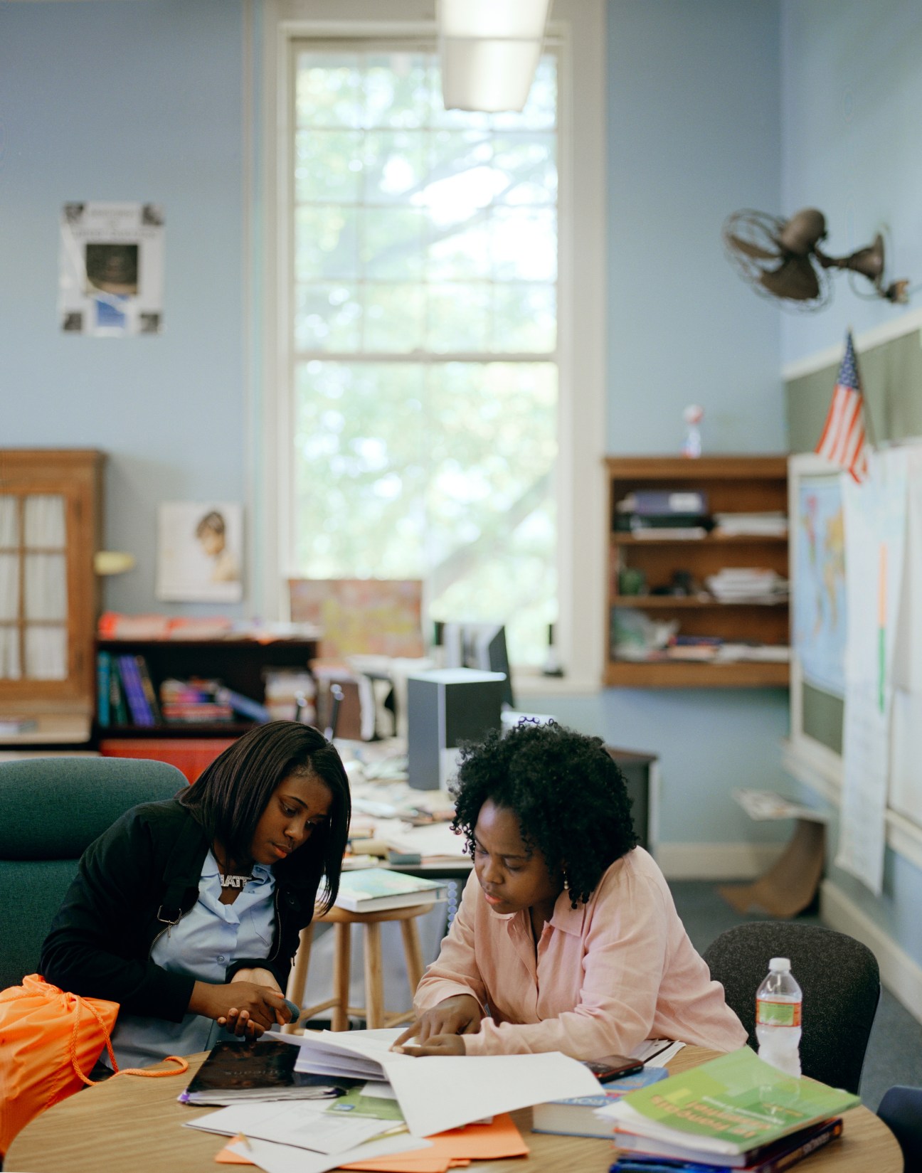 French teacher Diana Pierre-Louis works with a student at a desk in a bright classroom.