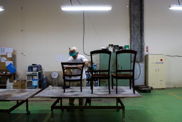 A factory worker inspects wooden chairs on a work table in a Maruni production facility.