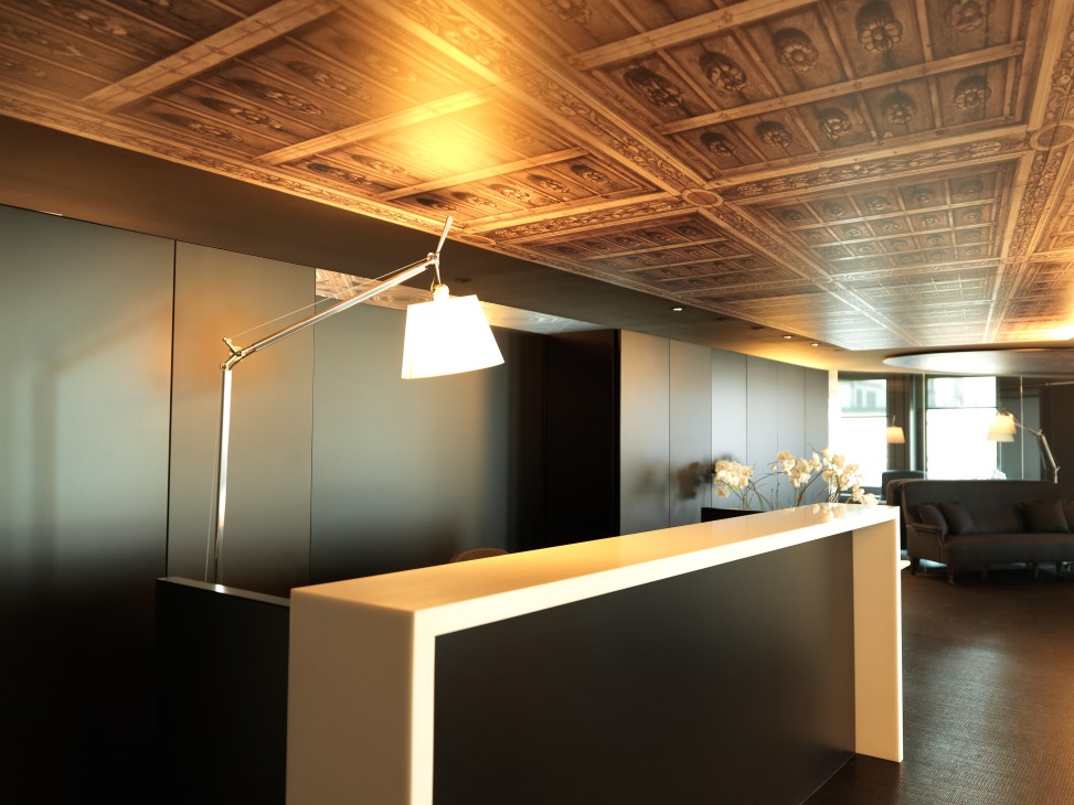Modern reception desk with white lamp and ornate wooden ceiling in IJ Partners Geneva office.