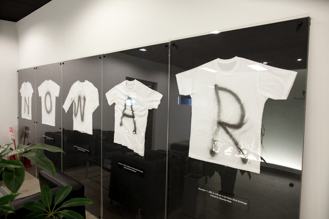 White t-shirts displayed in glass cases with spray-painted text spelling out messages.