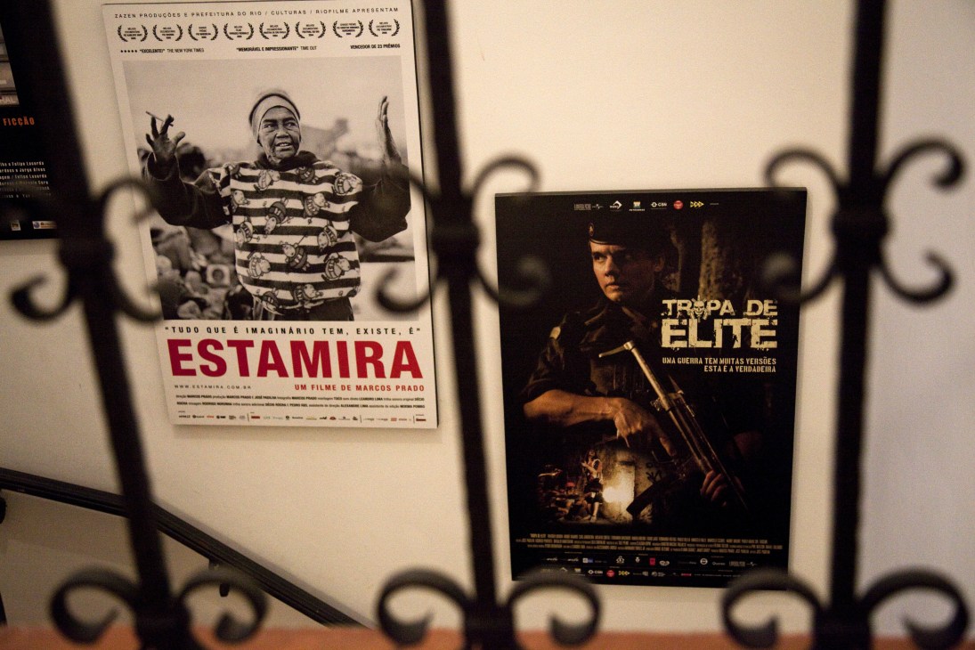 Movie posters for 'Estamira' and 'Tropa de Elite' displayed on a white wall behind ornate metal railings.