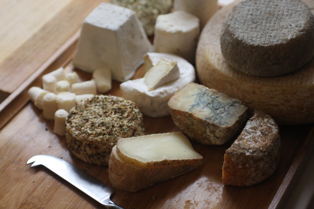 An assortment of artisan cheeses from Le Fromager de Pekin displayed on a wooden board with a knife.