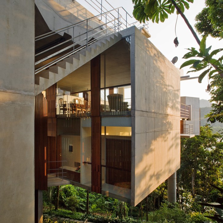 Modern concrete and wood house elevated on pillars among dense forest with large windows overlooking jungle and beach.