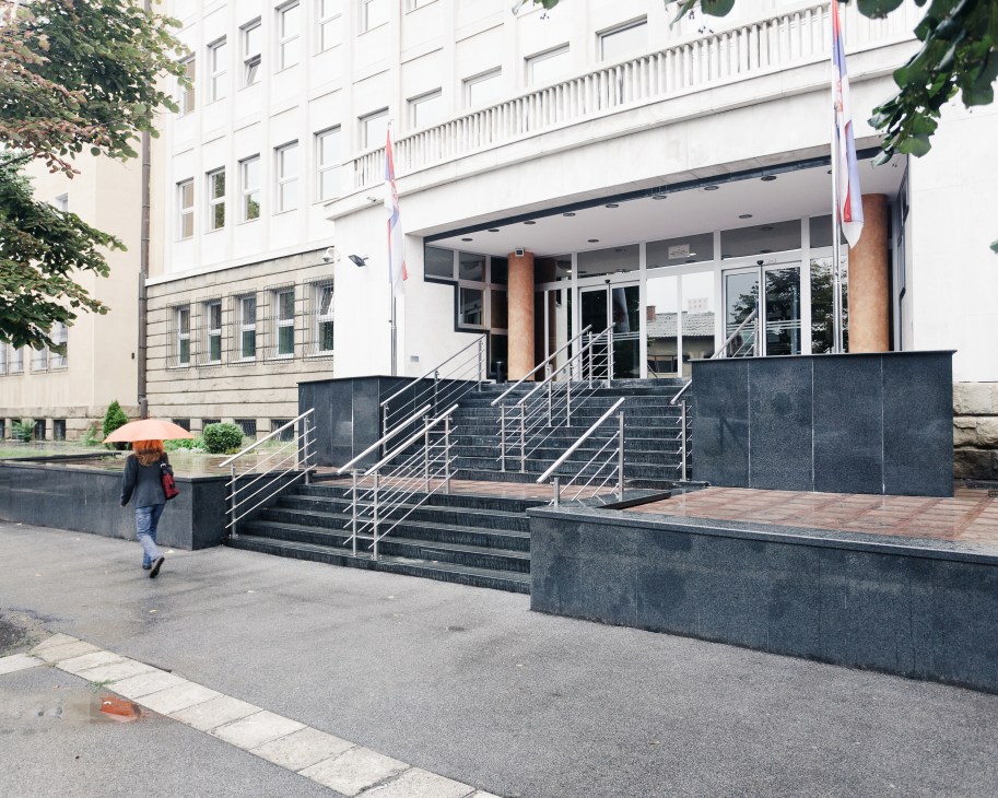 Modern institutional building entrance with metal railings, stairs, and flags, where Serbian war crimes prosecutor Vladimir Vukcevic's office is located.