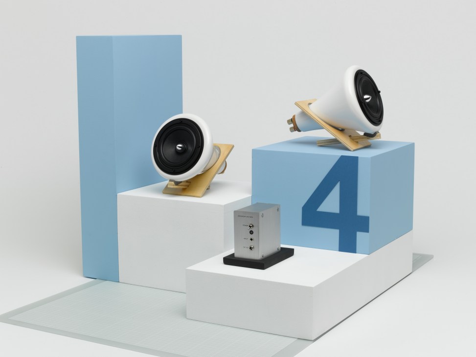 Joey Roth ceramic speakers made of porcelain, cork and Baltic birch displayed on white platforms with blue geometric backdrop.