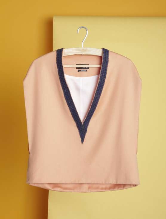 Peach sleeveless blouse with navy trim on hanger against yellow background.