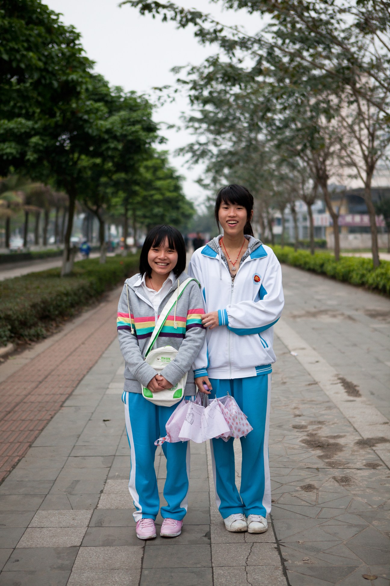 Two schoolgirls smile while standing on a tree-lined pedestrian path in Haikou, Hainan.