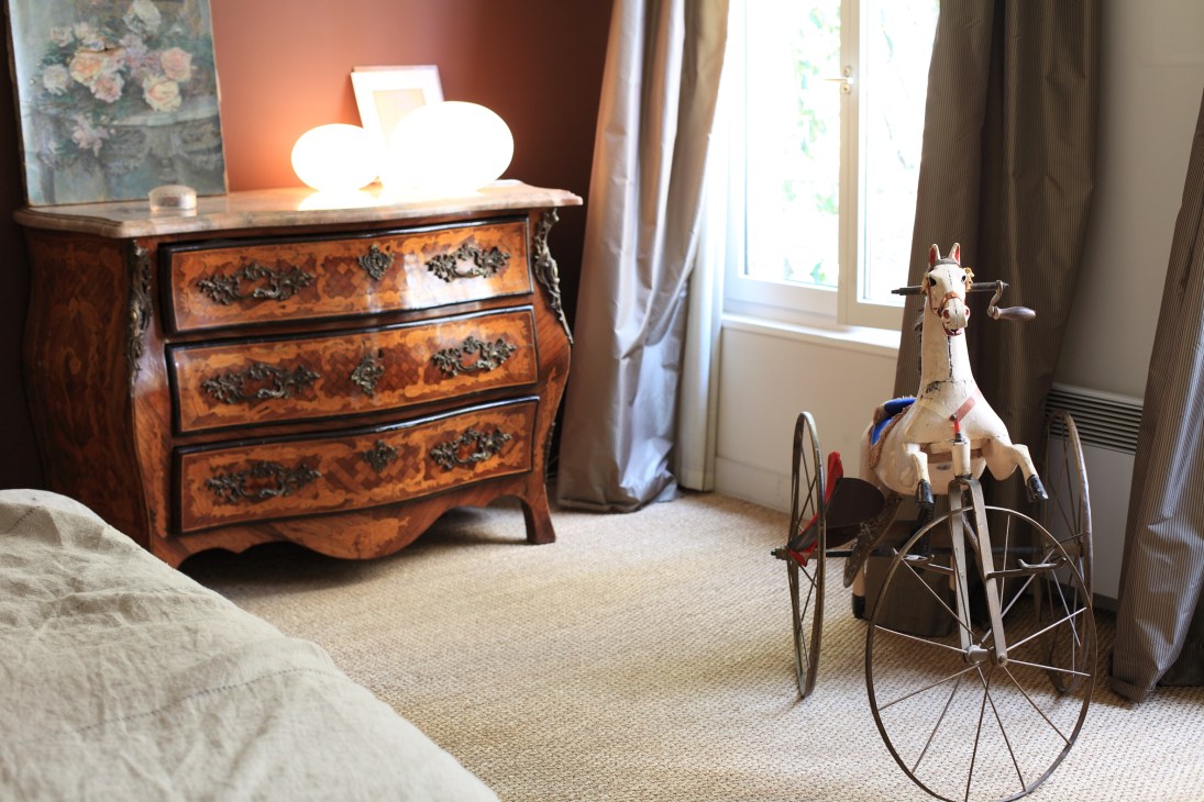 Vintage-inspired bedroom with ornate wooden dresser, decorative giraffe toy on tricycle, and warm lighting at Hotel Eldorado.
