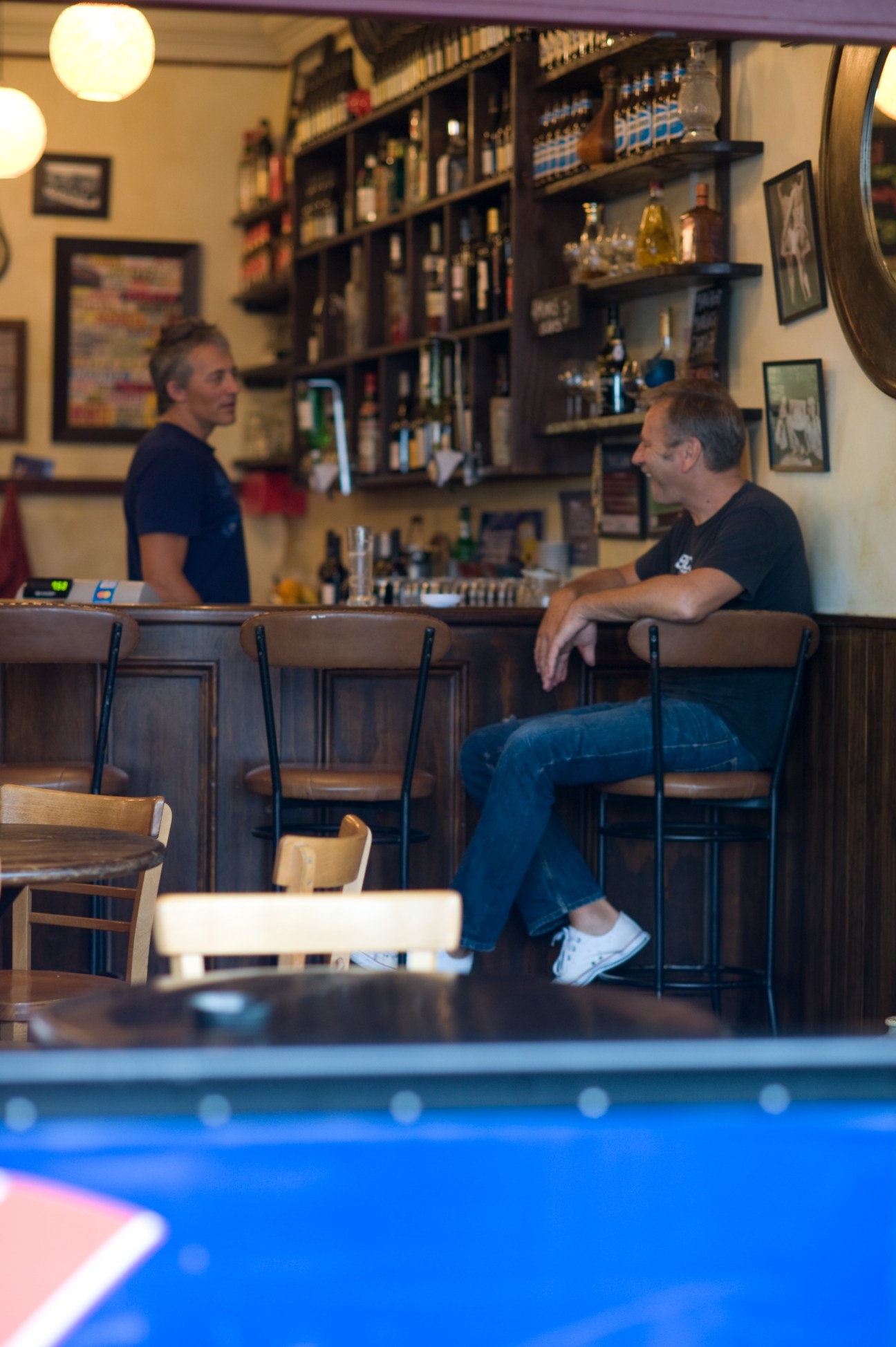 Two men at a bar counter with shelves of bottles behind them at Mondial wine bar.