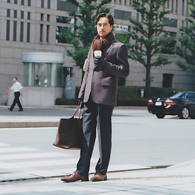 Man in business attire holding a beverage and Bottega Veneta bag on urban street.
