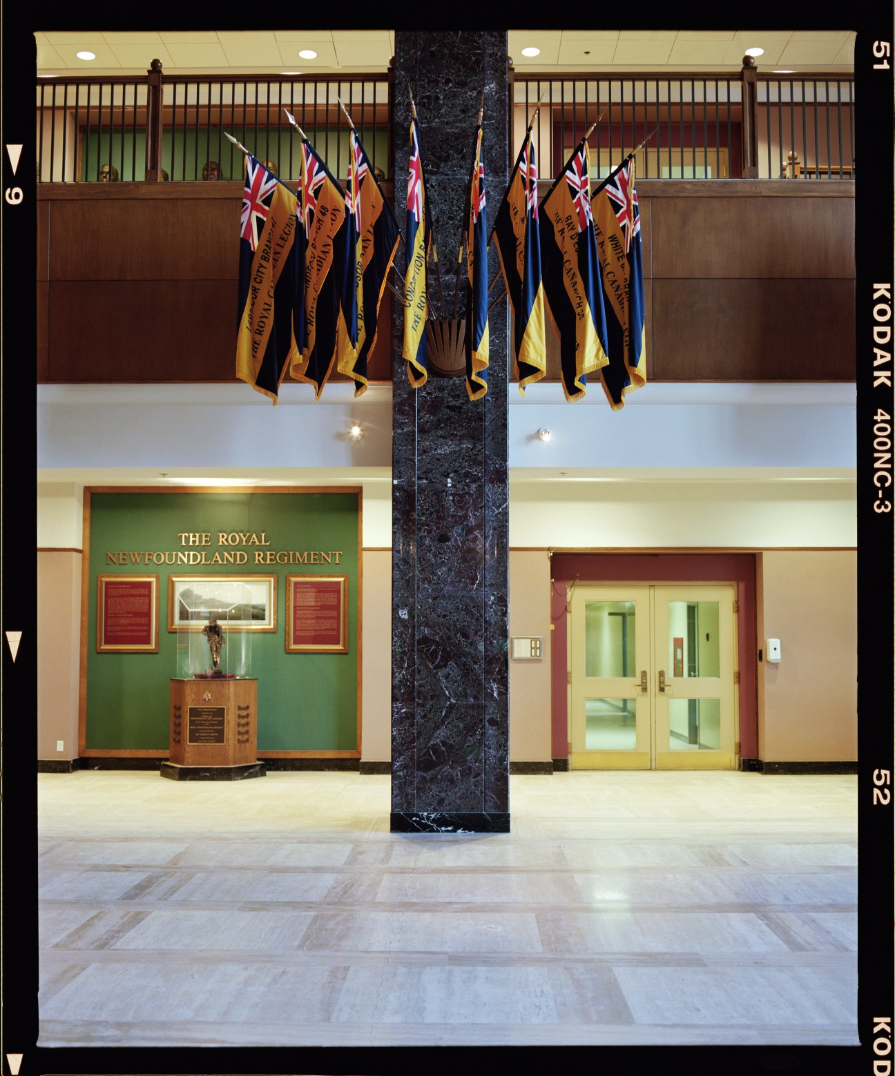 The Confederation Building lobby with Royal Newfoundland Regiment flags and insignia displayed on green wall.