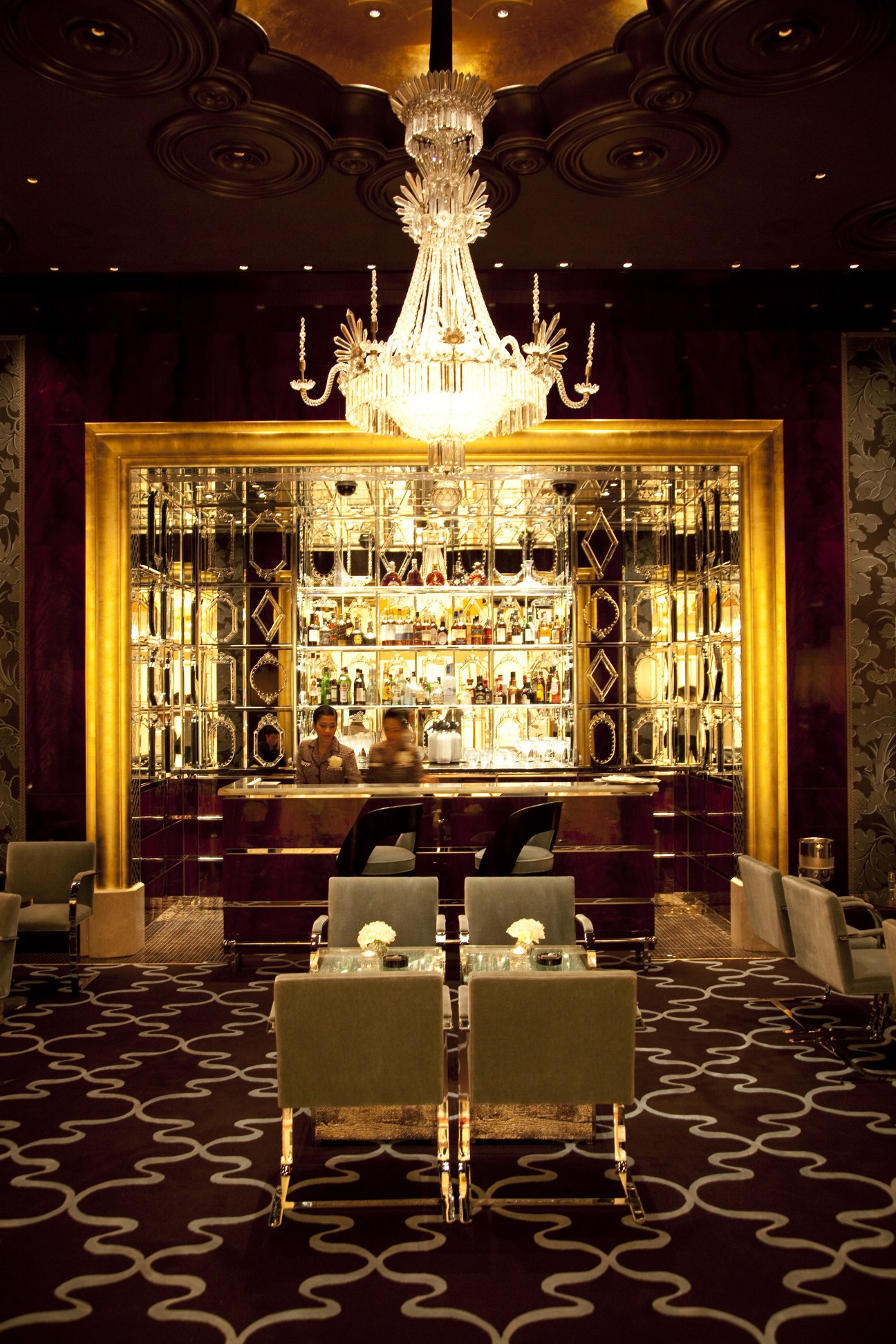 Luxurious bar interior at Wynn Resort Macau with crystal chandelier, gold-framed shelving, and upholstered seating.
