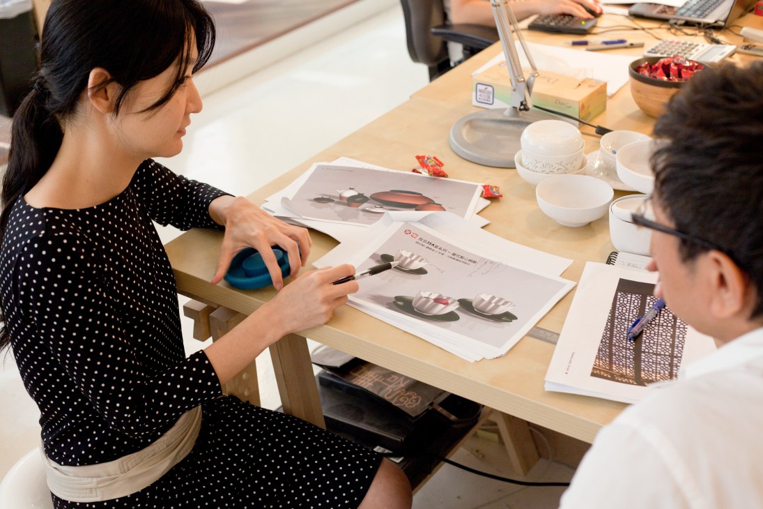 Jia Inc employees reviewing design sketches and product samples at a wooden desk in their Kowloon headquarters.