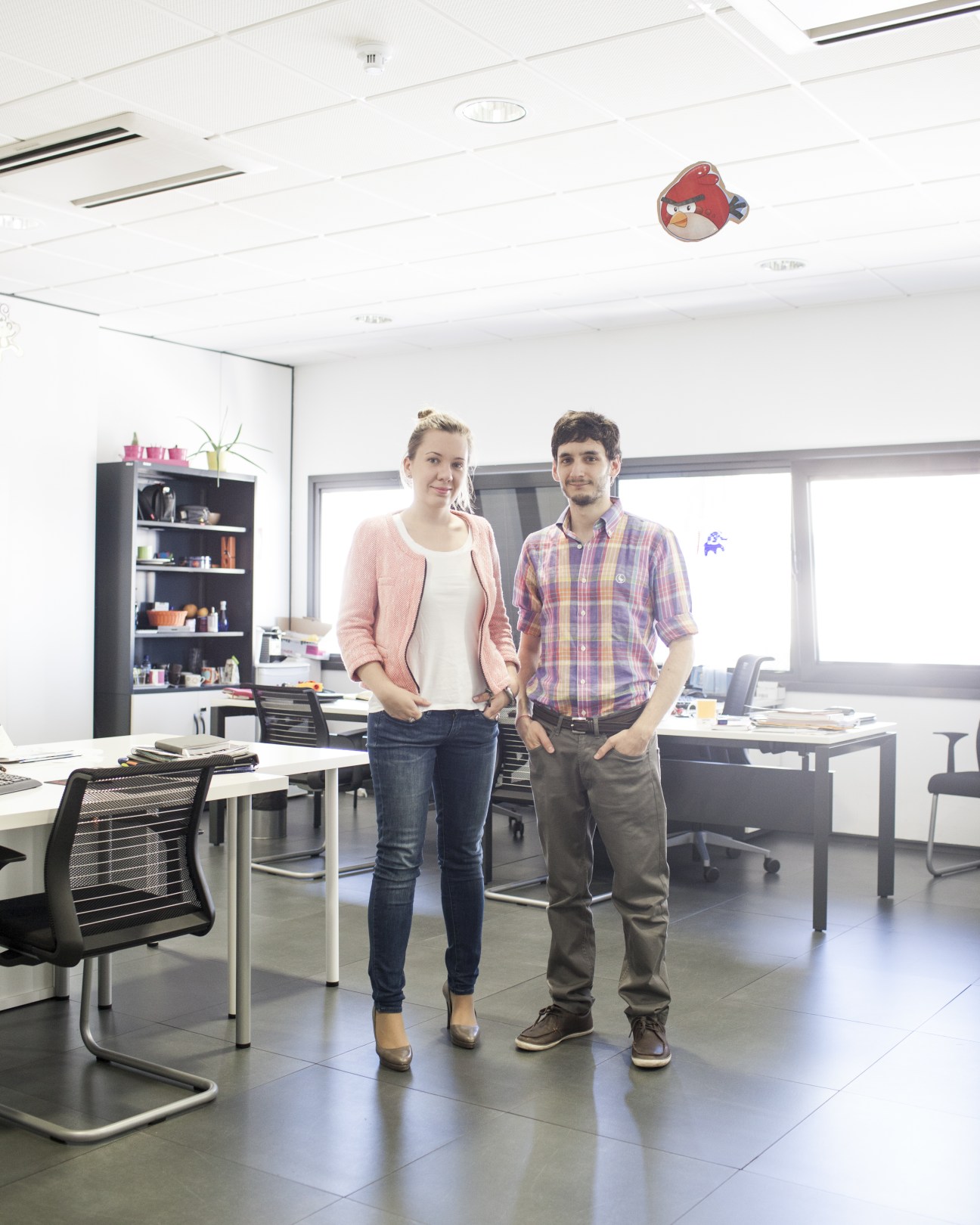 Two entrepreneurs stand in a modern office space with desks and shelving at Madrid Emprende.