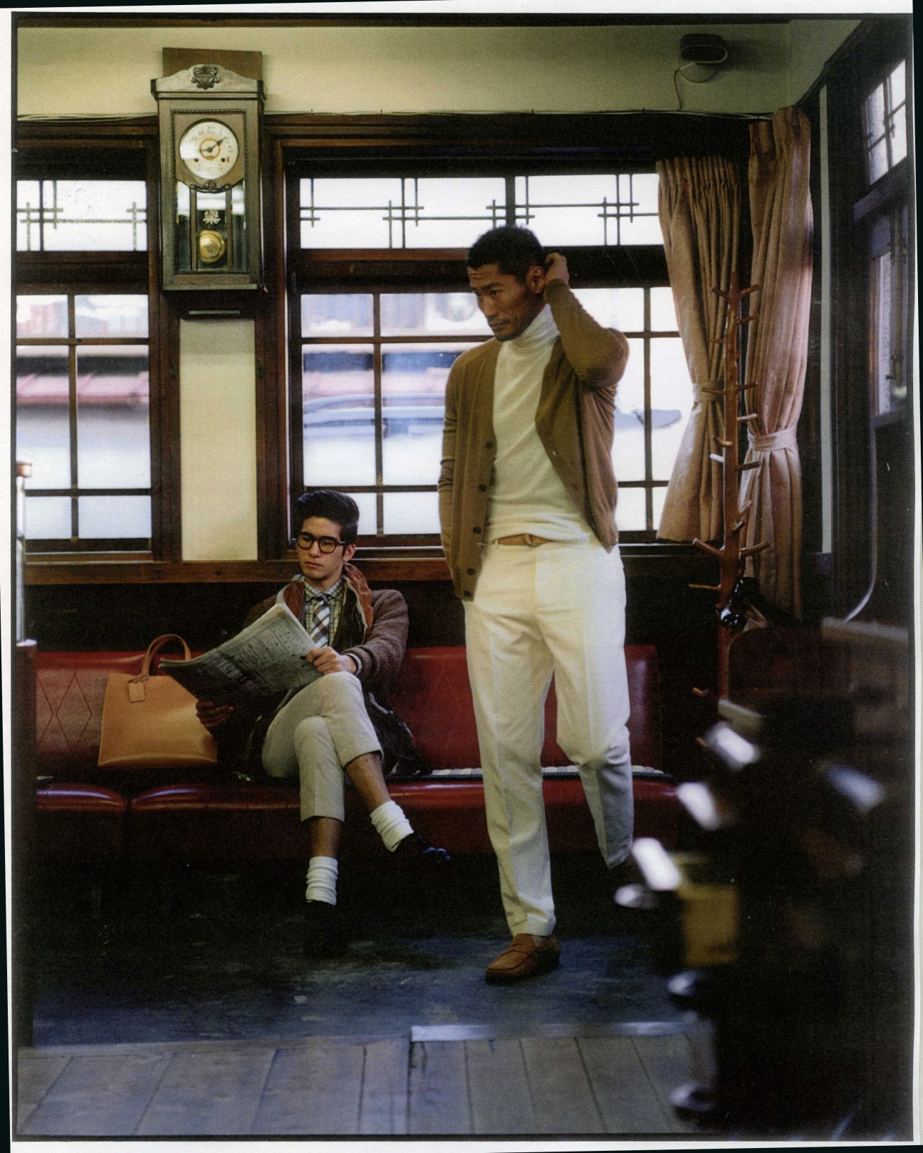 Two men posed in a traditional Tokyo barber shop interior with vintage clock and gridded windows.