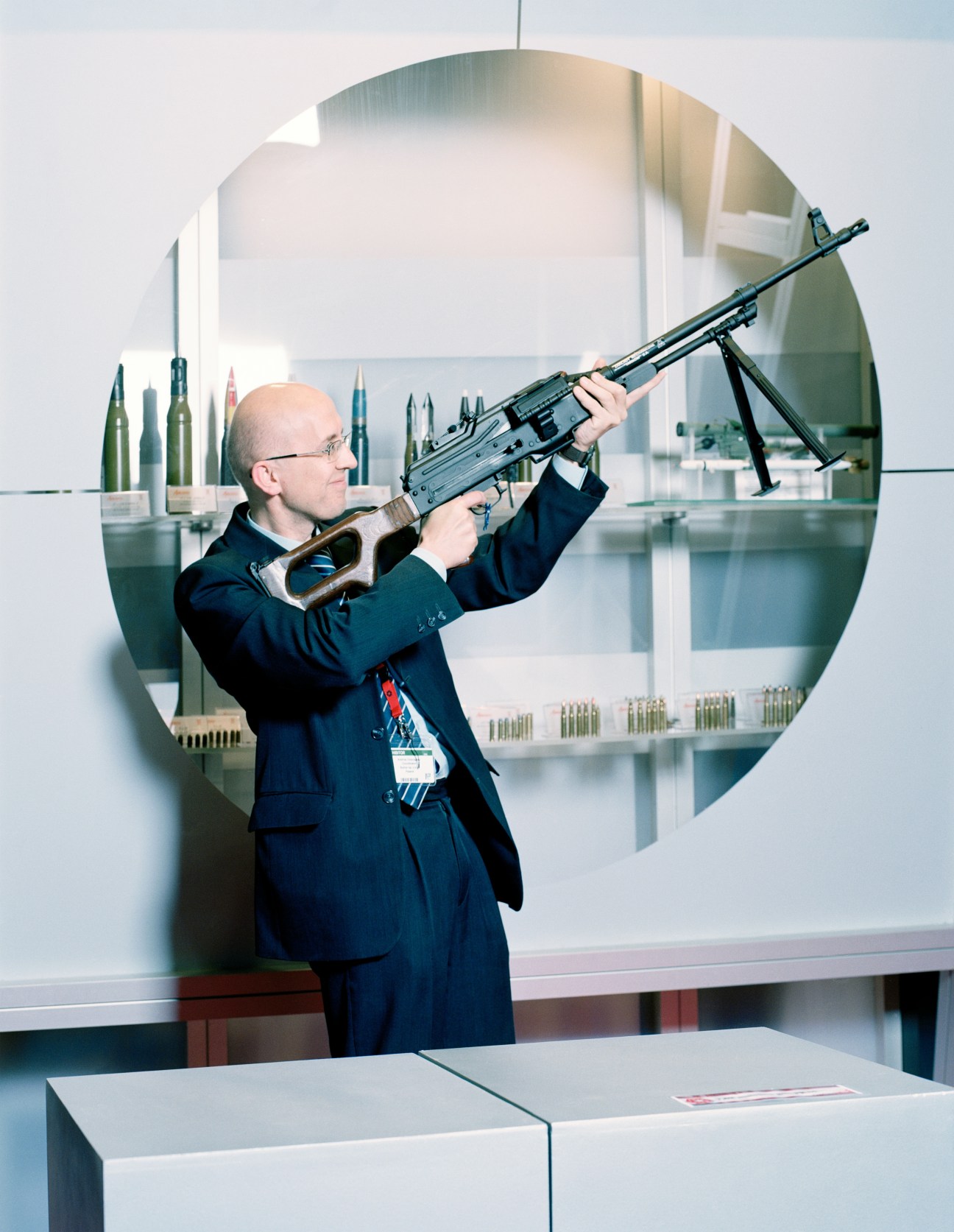 Man in business suit holds a PKM lightweight machine gun at arms fair exhibition.