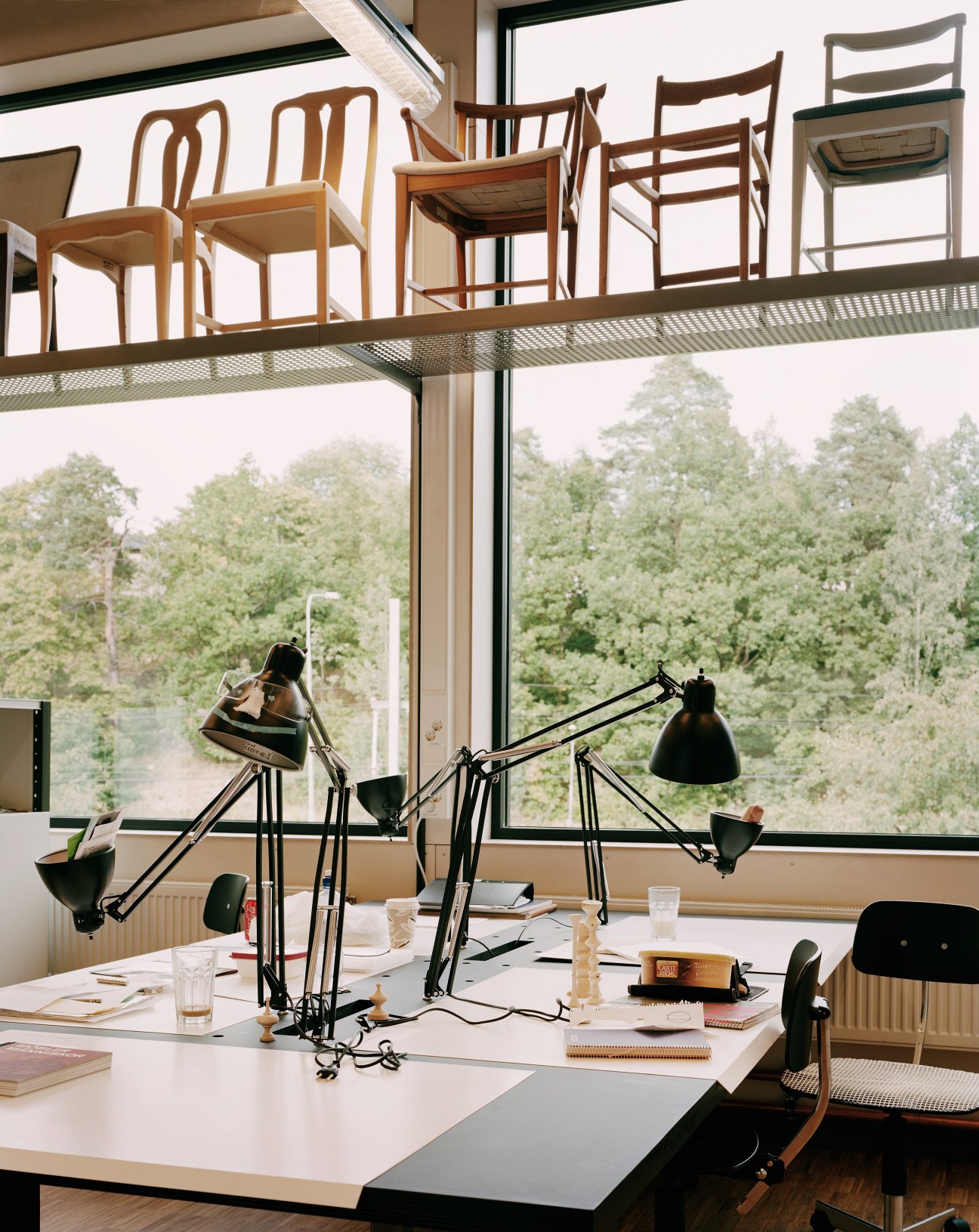 Classroom workspace at Carl Malmsten Furniture Studies school with wooden chairs, black task lamps and forest view.