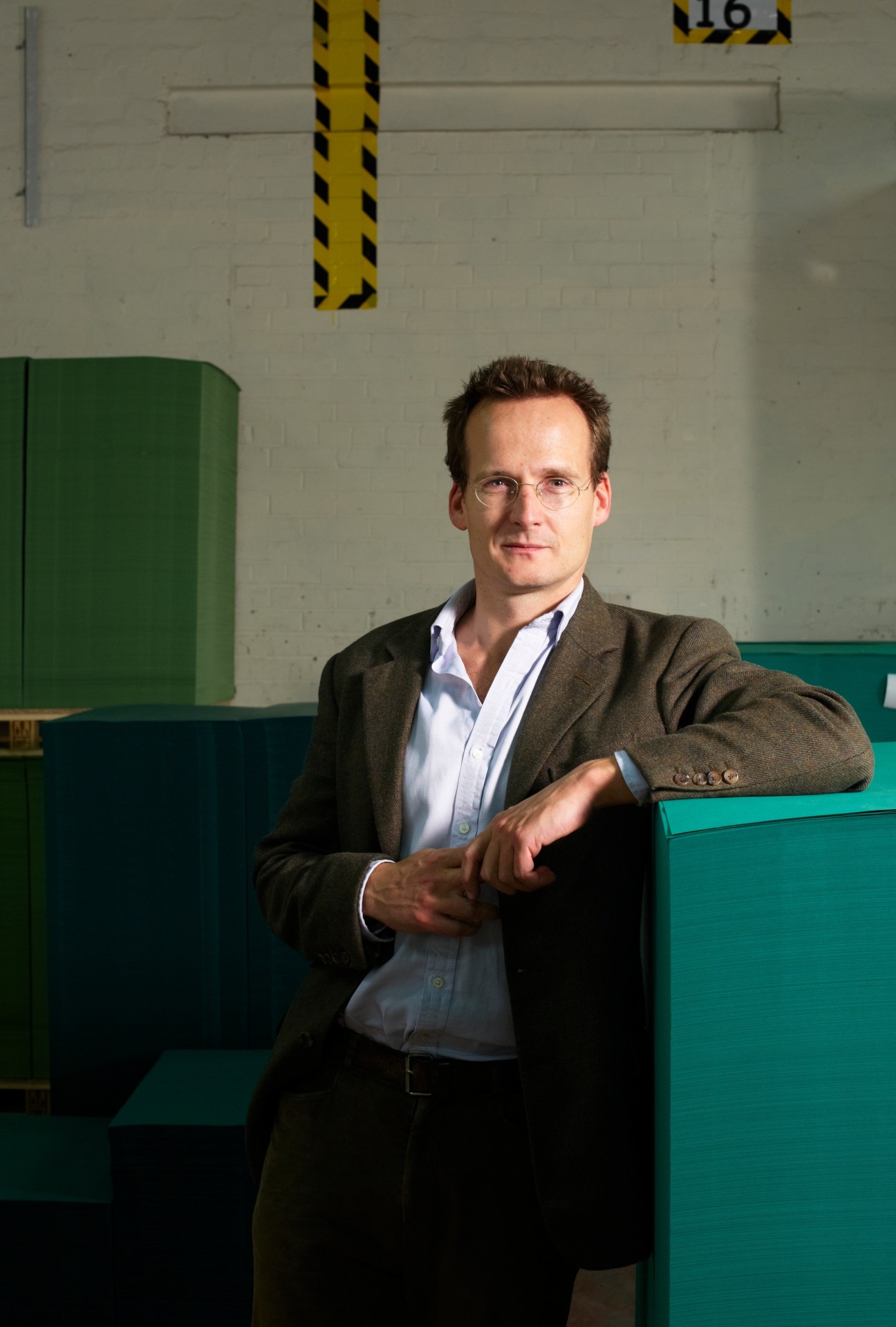Portrait of Mark Cropper, chairman of James Cropper paper manufacturer, wearing glasses and brown blazer against industrial background.