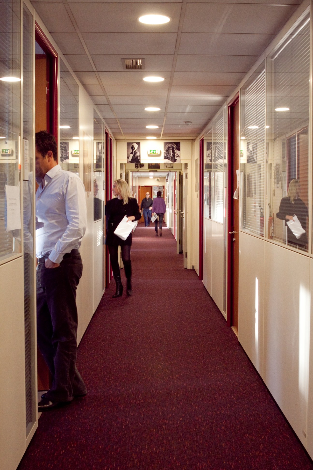Office corridor at Paris Match with staff members walking past glass-walled offices with burgundy doors.
