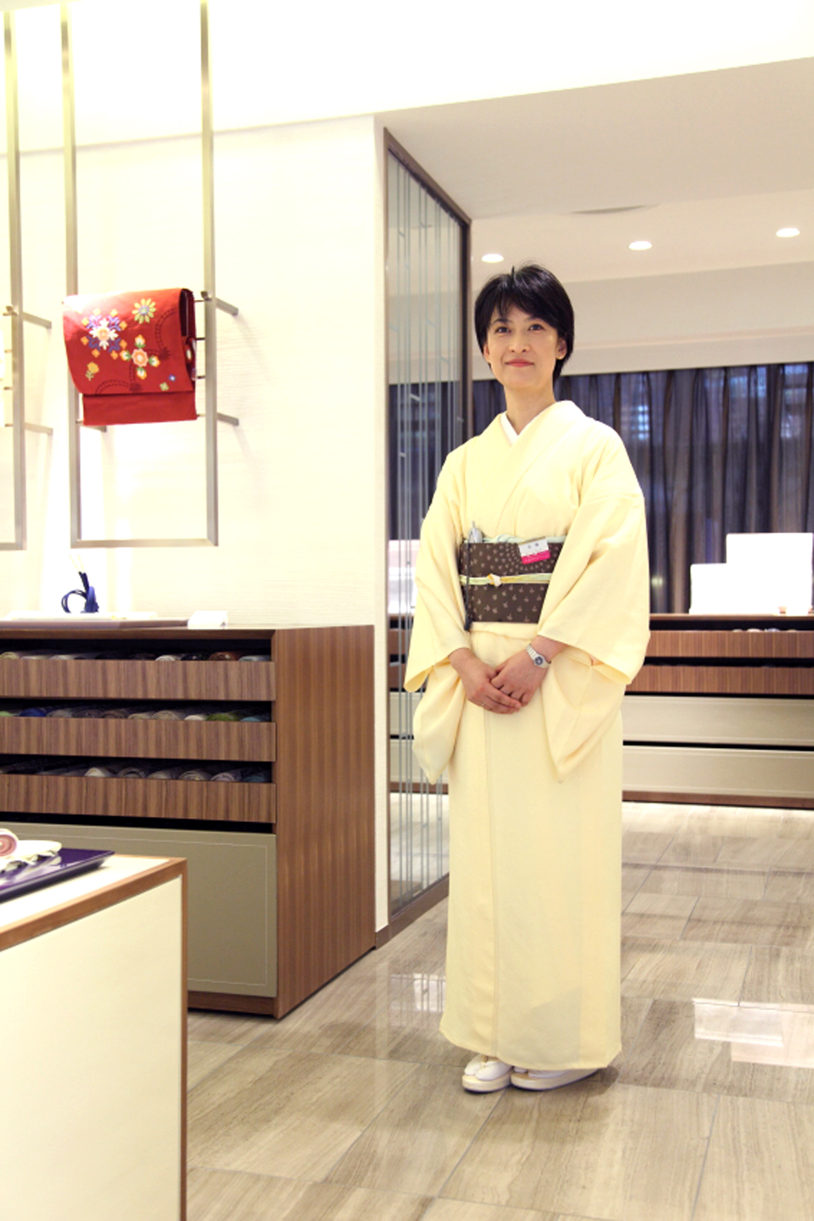Woman in pale yellow kimono standing in modern Mitsukoshi department store interior with wooden counters.