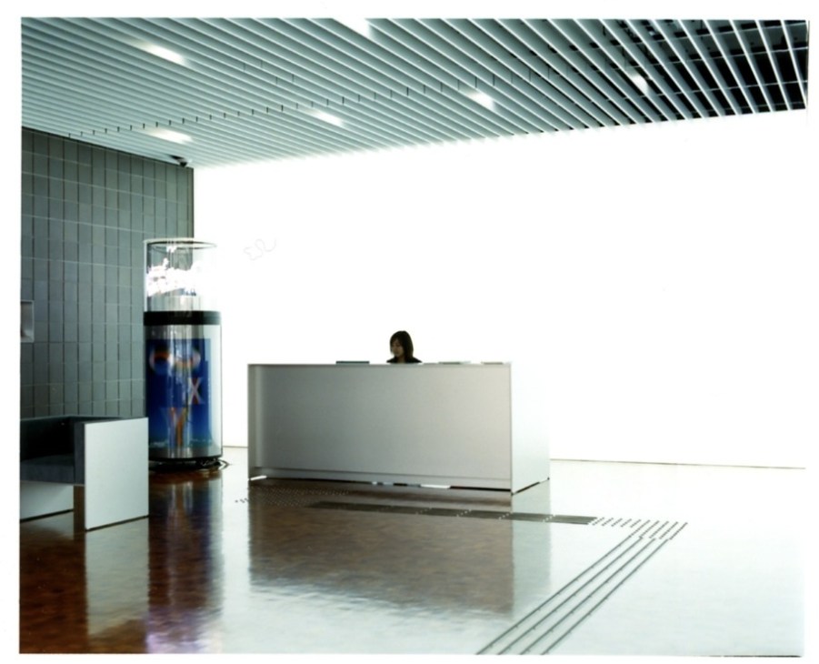 Modern minimalist lobby with reception desk, angular ceiling design, and polished floor at Morisawa's Osaka headquarters.