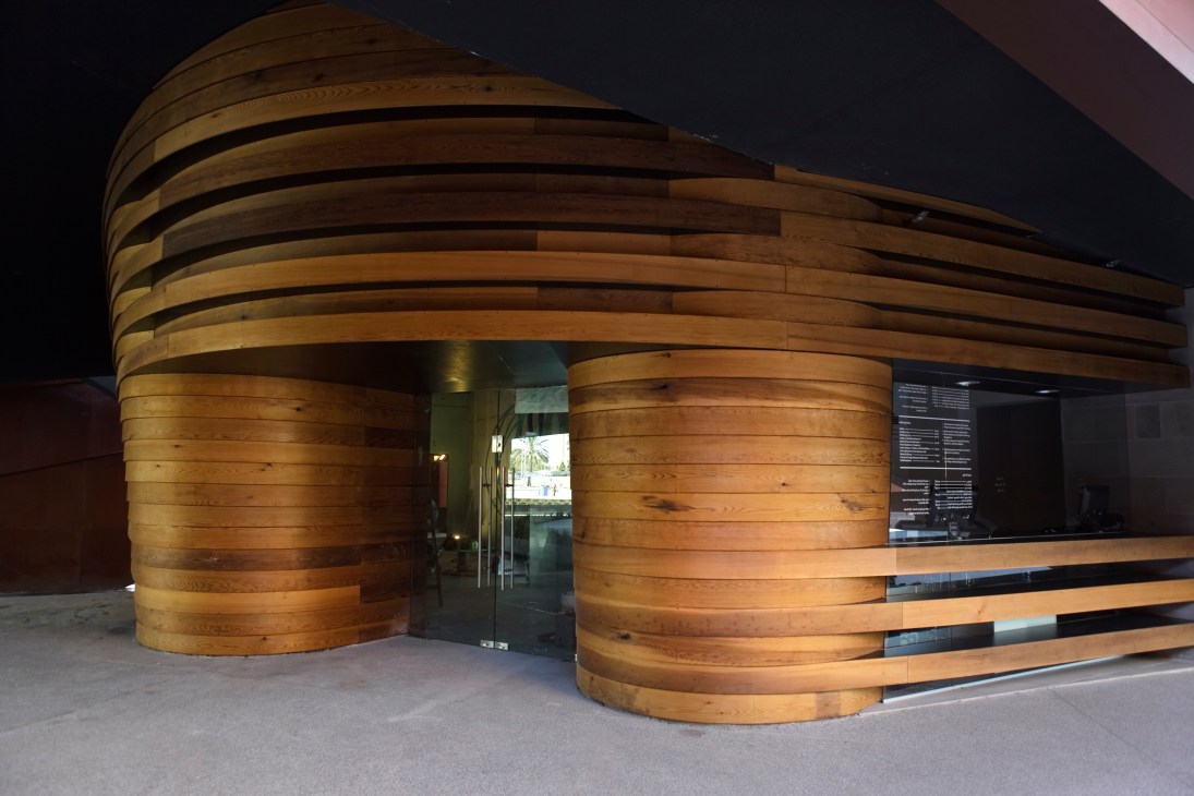 Wooden curved entrance structure with horizontal bands to the Design Museum Holon café and shop.