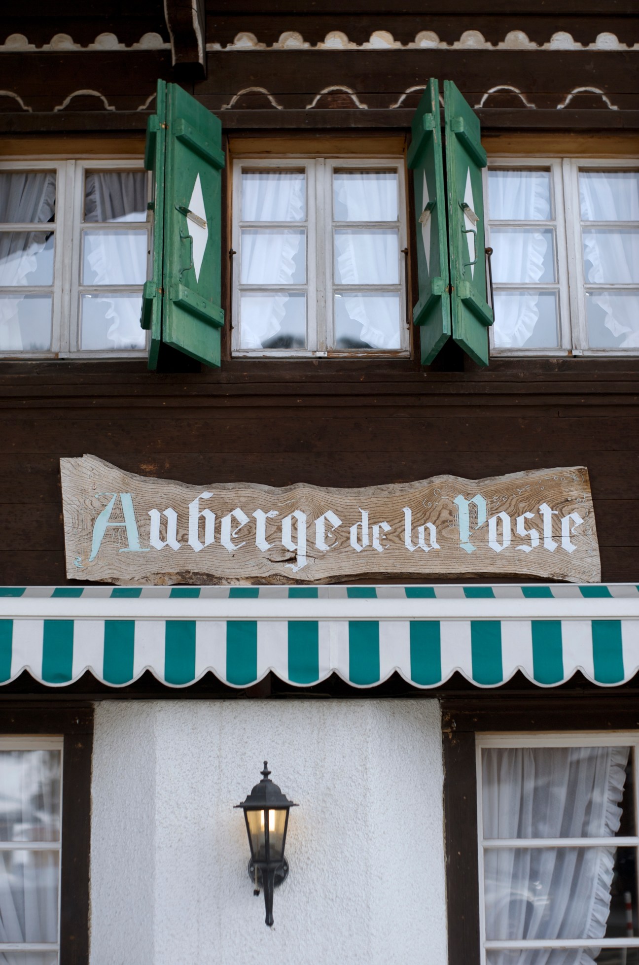 Exterior of Auberge de la Poste alpine restaurant with green shutters and striped awning.