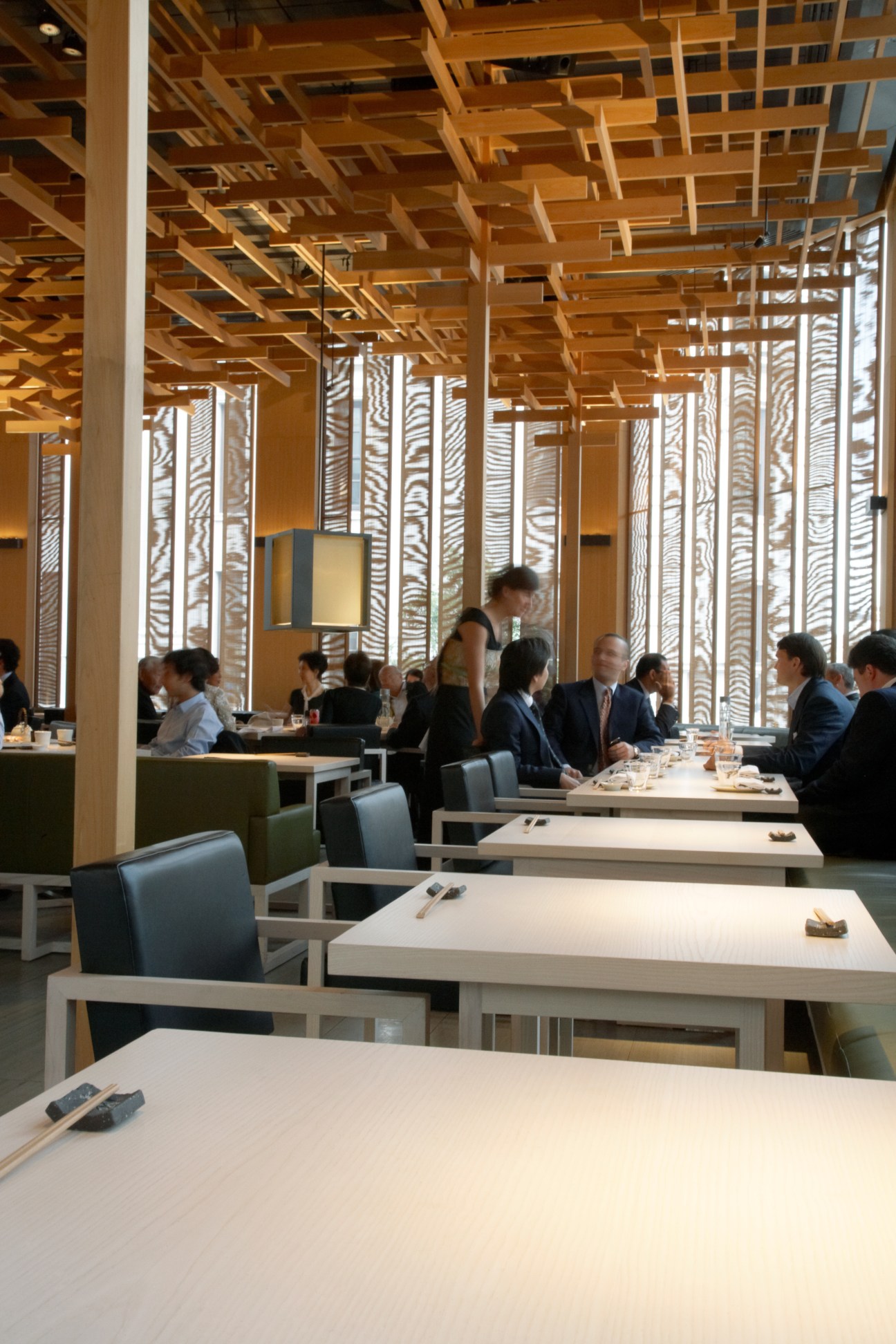 Interior of Saké no Hana restaurant showing minimalist dining room with communal tables and wooden lattice screens.