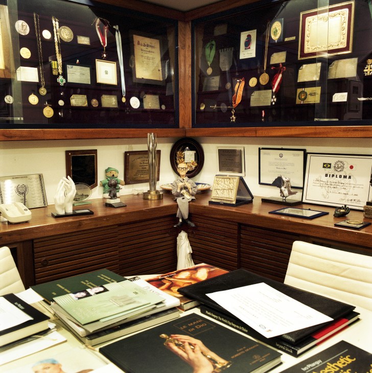 Display cabinets and desk in Dr. Ivo Pitanguy's clinic office showcasing awards, medals, diplomas, and gifts from patients.