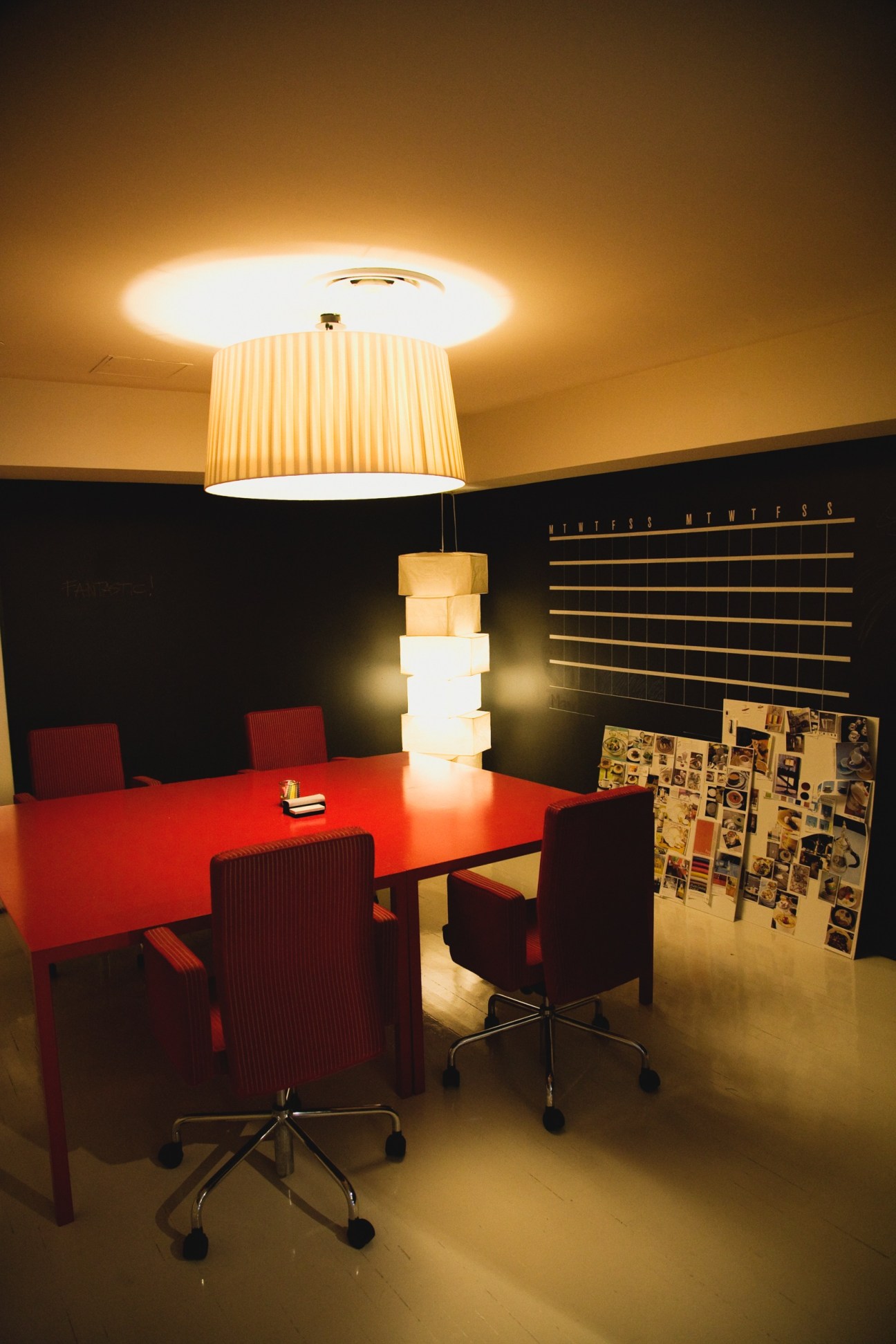 Meeting room with red table, burgundy chairs, striped pendant lamp, and mood board on wall.