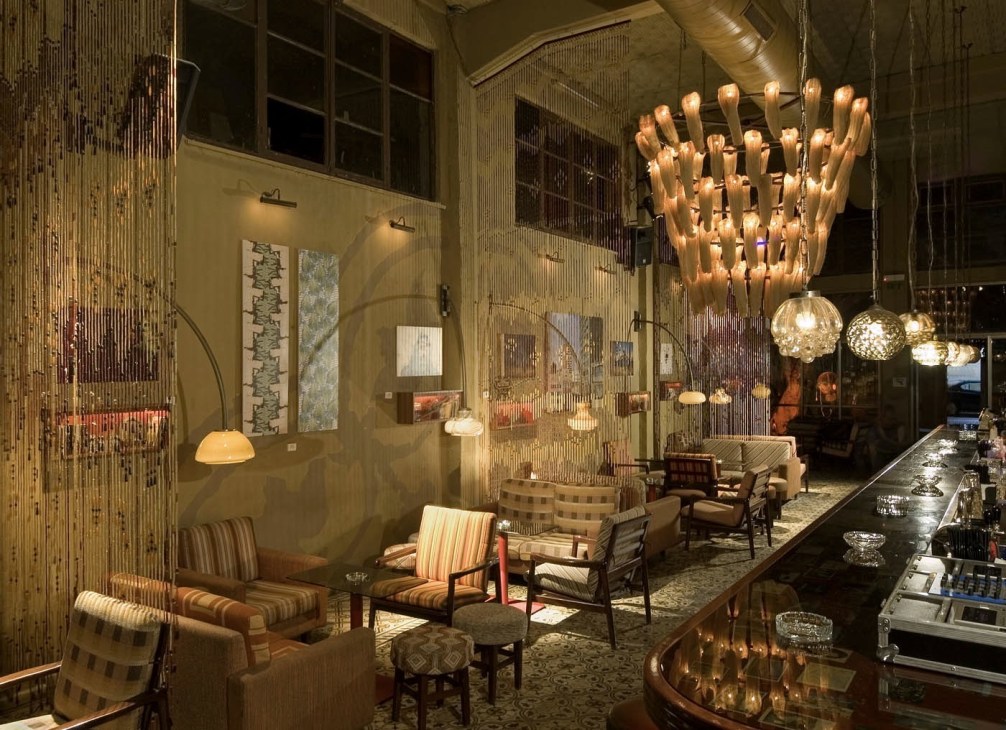 Saloona bar interior with copper and glass pendant lighting, striped upholstered chairs, and bar counter at night.