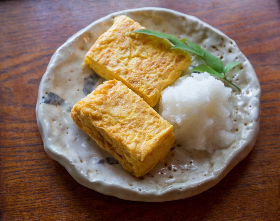 Japanese omelette (tamago yaki) with grated radish on a speckled ceramic plate