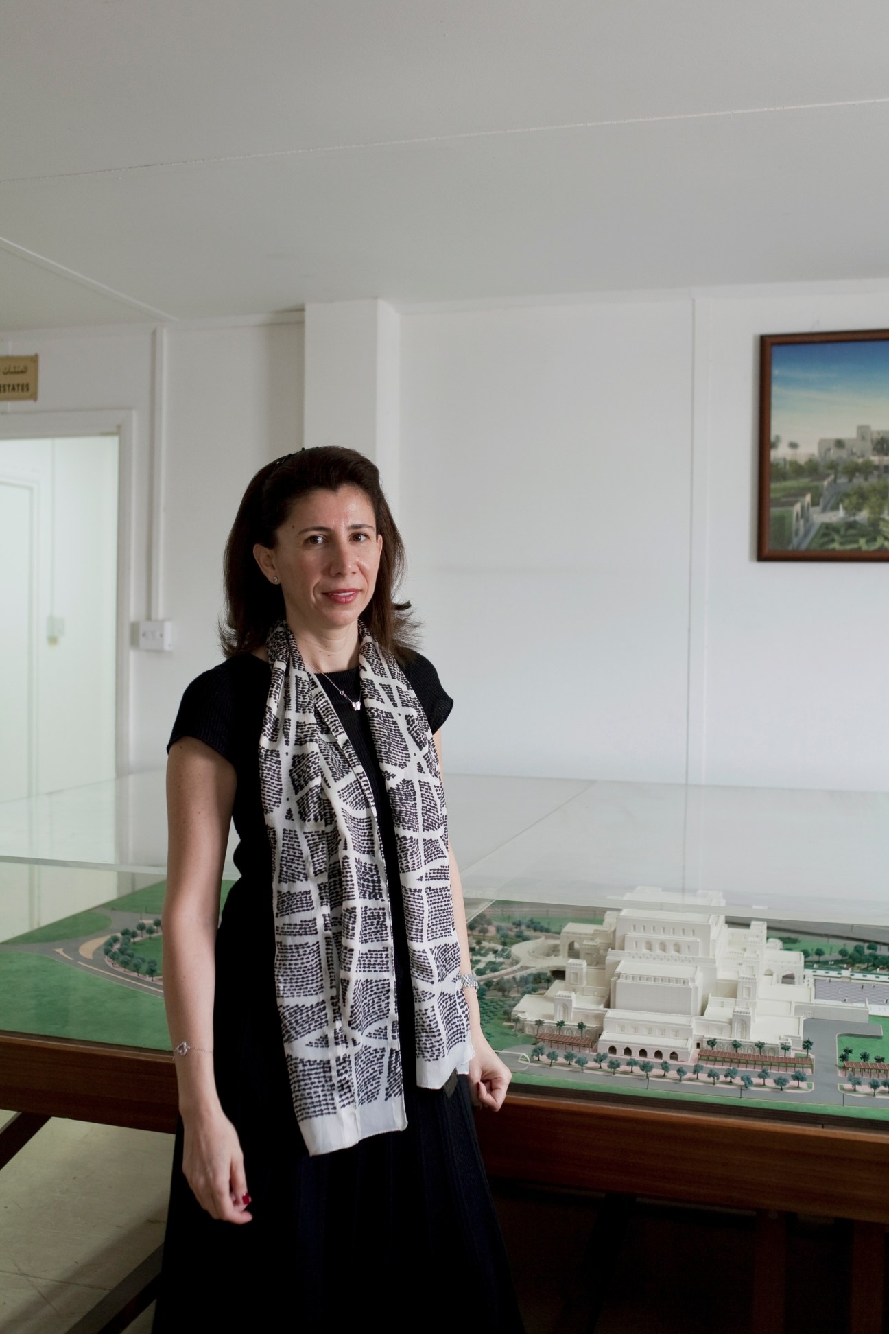 Iman Hindawi, director of the Royal Opera House, stands in a modern white interior next to an architectural model of the opera house building.